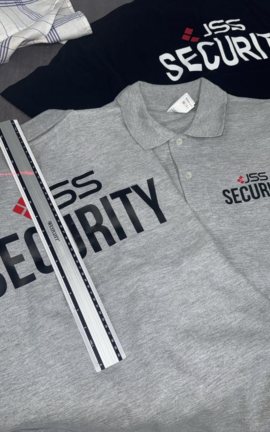 Graues Poloshirt mit Brustlogo eines Sicherheitsdienstes, daneben ein schwarzes Shirt mit Rückendruck