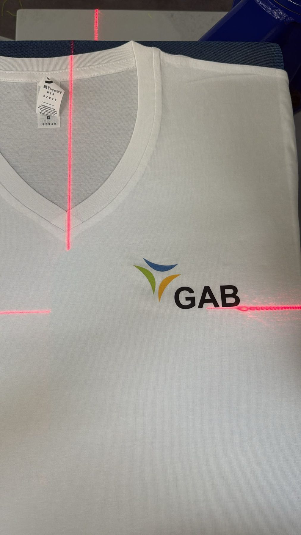 Weißes Shirt mit Firmenlogo auf der Brust, Positionierlaser zeigt die Ausrichtung