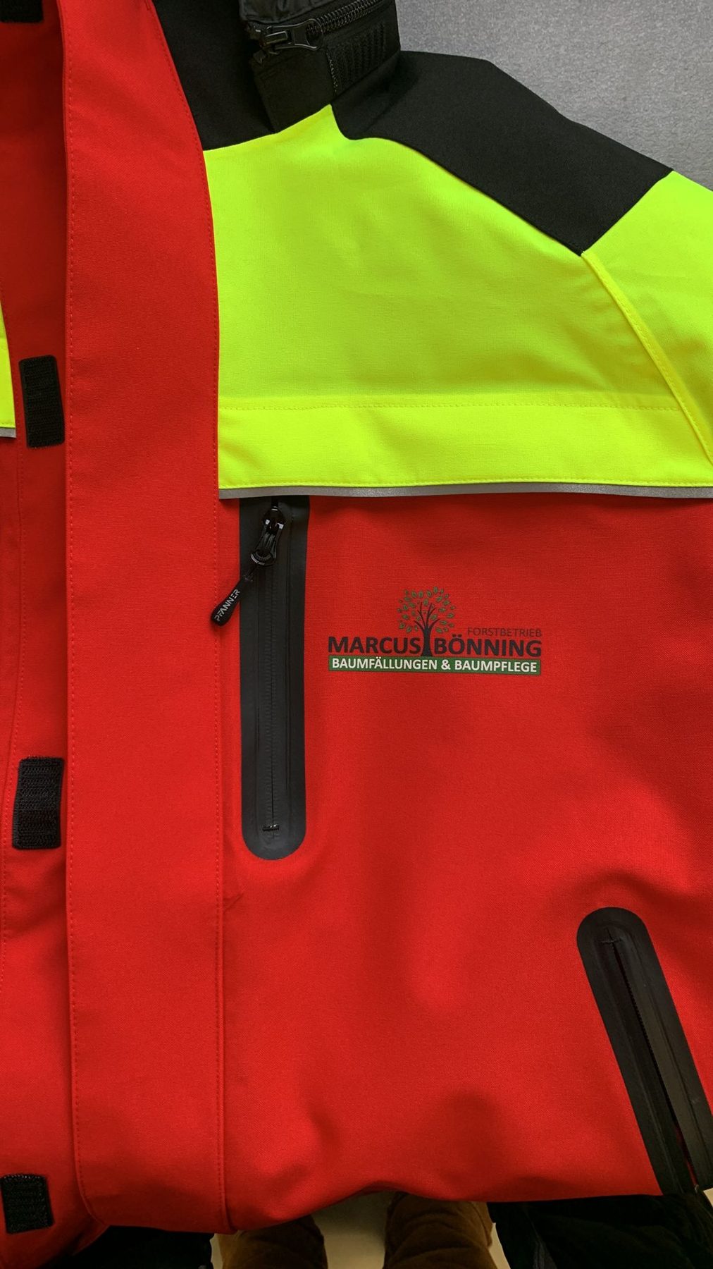 Rot-gelbe Warnschutzjacke mit gedrucktem Logo eines Forstbetriebs auf der Brust