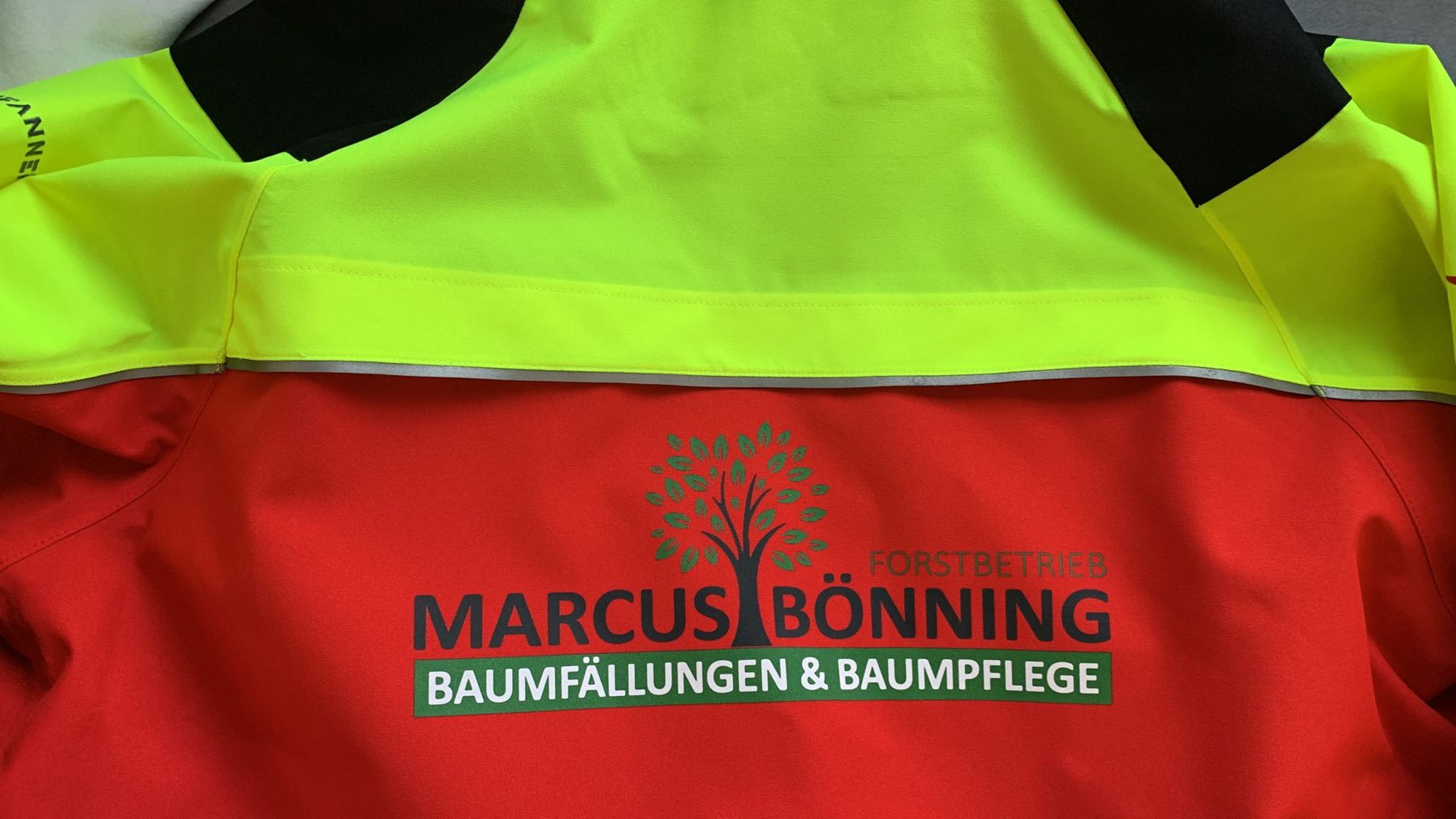 Rückseite einer rot-gelben Warnschutzjacke mit großem Firmendruck
