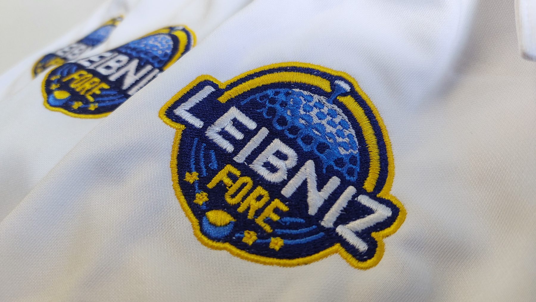 Gesticktes Vereinslogo in Blau und Gelb auf einem weißen Poloshirt