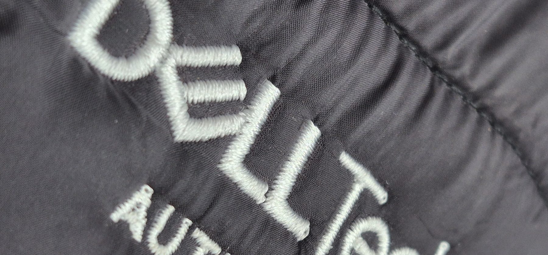Weißer gestickter Schriftzug auf einer dunklen Steppjacke